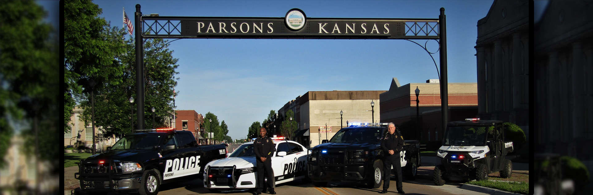 Welcome to Parsons Kansas sign featuring police vehicles and officers standing beneath it.